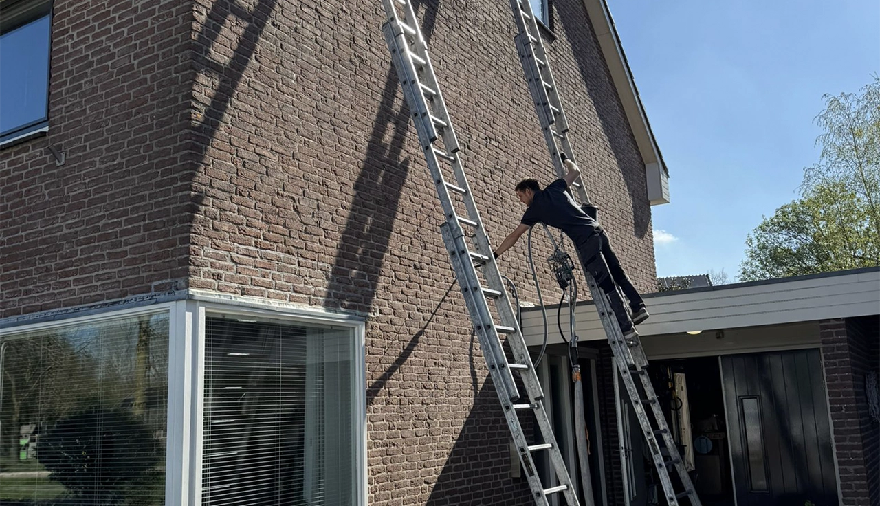 Monteur brengt spouwmuurisolatie aan bij een woning met bakstenen gevel voor betere isolatie en lagere energiekosten.